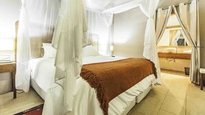 A bedroom with a four-poster bed, a wooden headboard, and a large window with curtains.