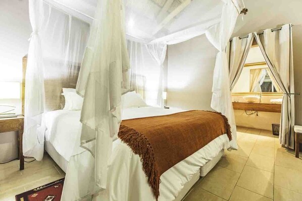 A bedroom with a four-poster bed, a wooden headboard, and a large window with curtains. - Zalala Beach Lodge (Quelimane)
