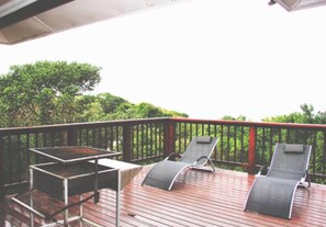 A wooden deck with two lounge chairs and a metal table. - Campismo Ninho 29 (Ponta d'Ouro)