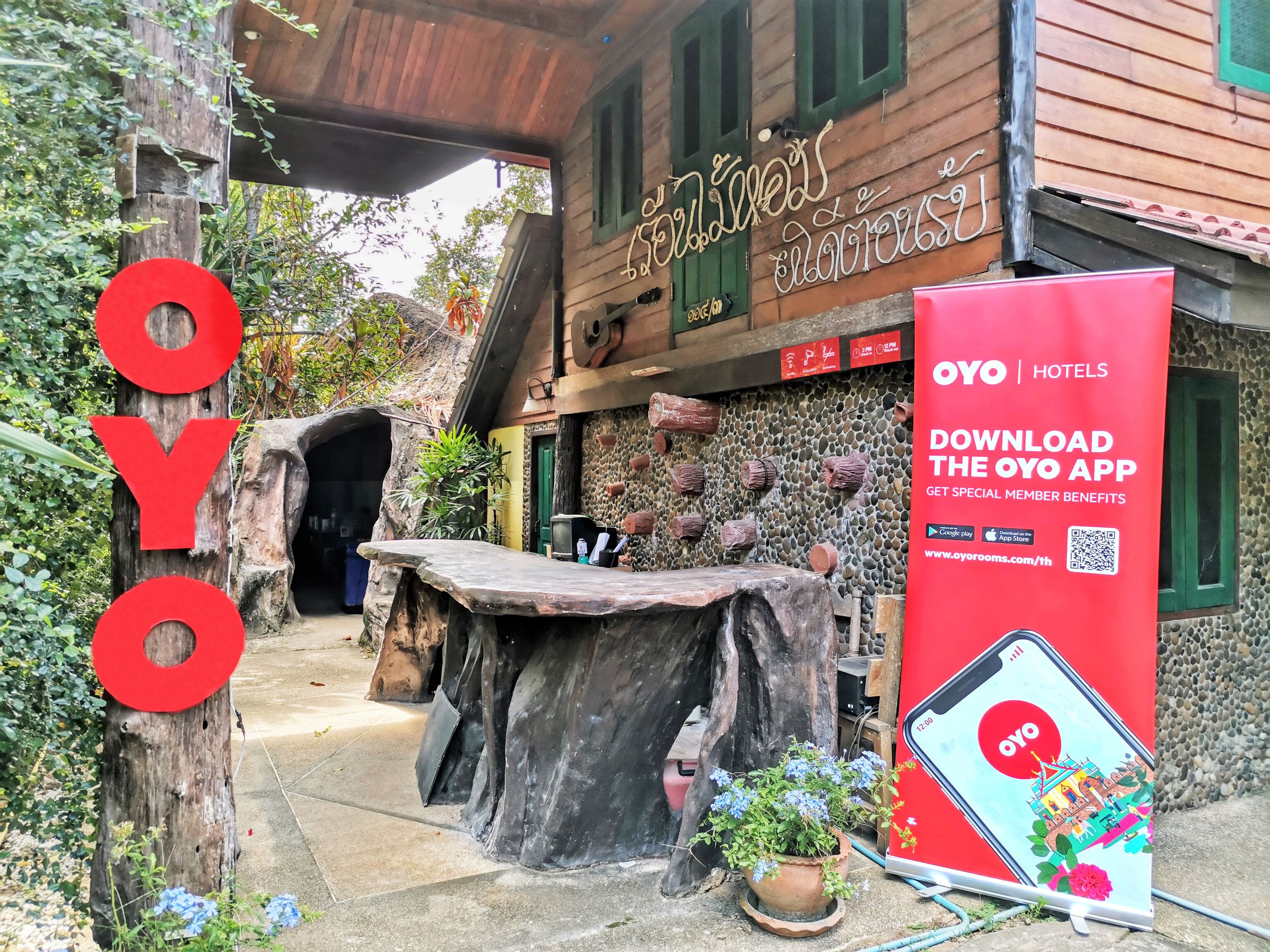 A hotel entrance with a wooden facade, a stone wall, and a red sign advertising the OYO app.
