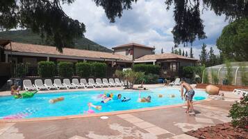 Un espace piscine comprenant des chaises longues, une piscine et un bâtiment doté d’un toit en tuiles.