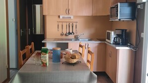 A compact kitchen with wooden cabinets, a microwave, a coffee maker, and a dining table with chairs.