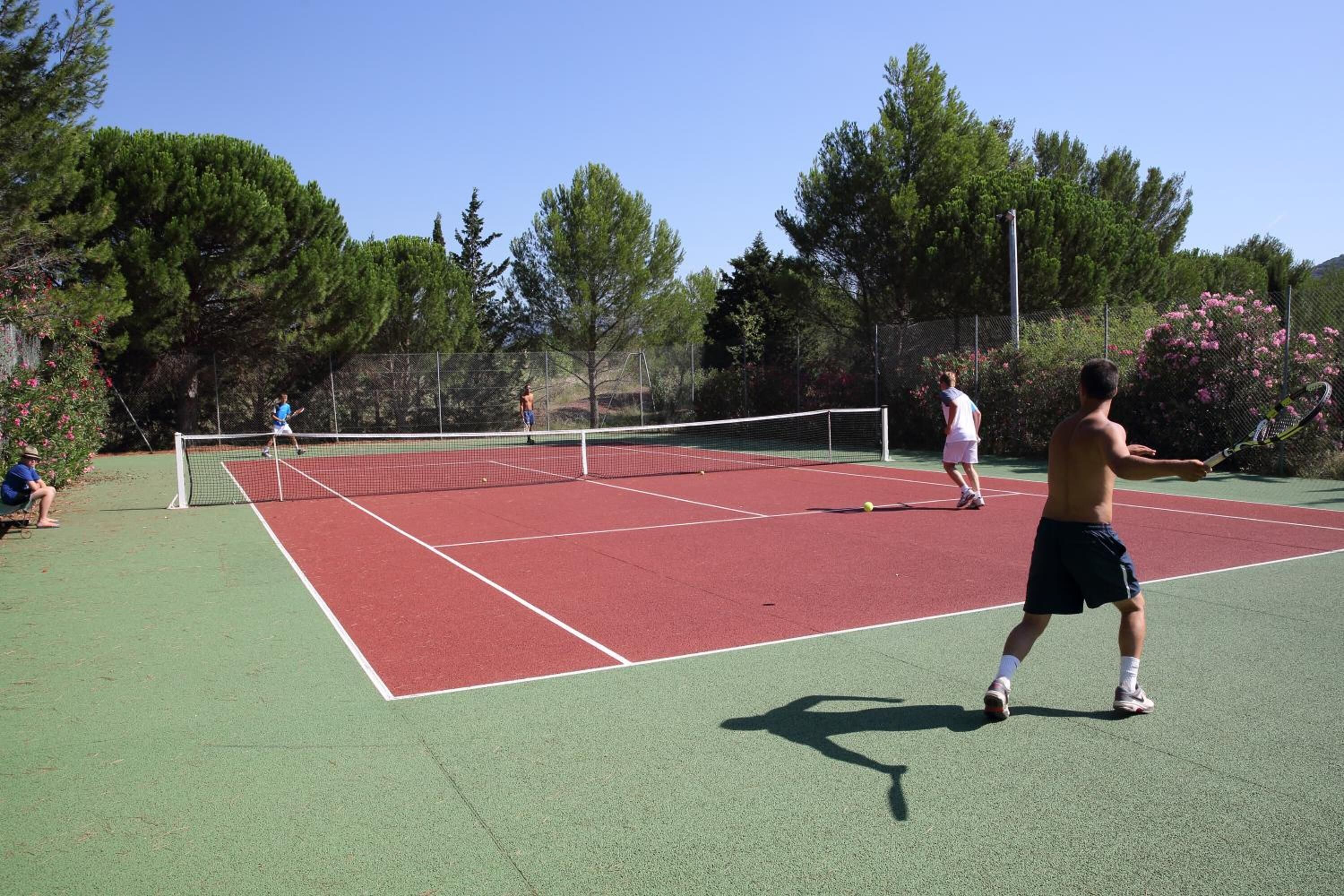 A tennis court with a net, surrounded by trees and a fence.
