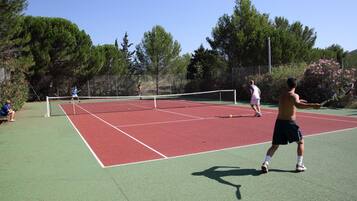 A tennis court with a net, surrounded by trees and a fence.