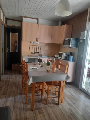Un comedor con una mesa lista para cuatro personas, sillas de madera, un microondas y un lavamanos.