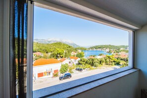 A view from a window overlooking a coastal town with buildings, a road, and a body of water. - Villa Teuta (Korcula)