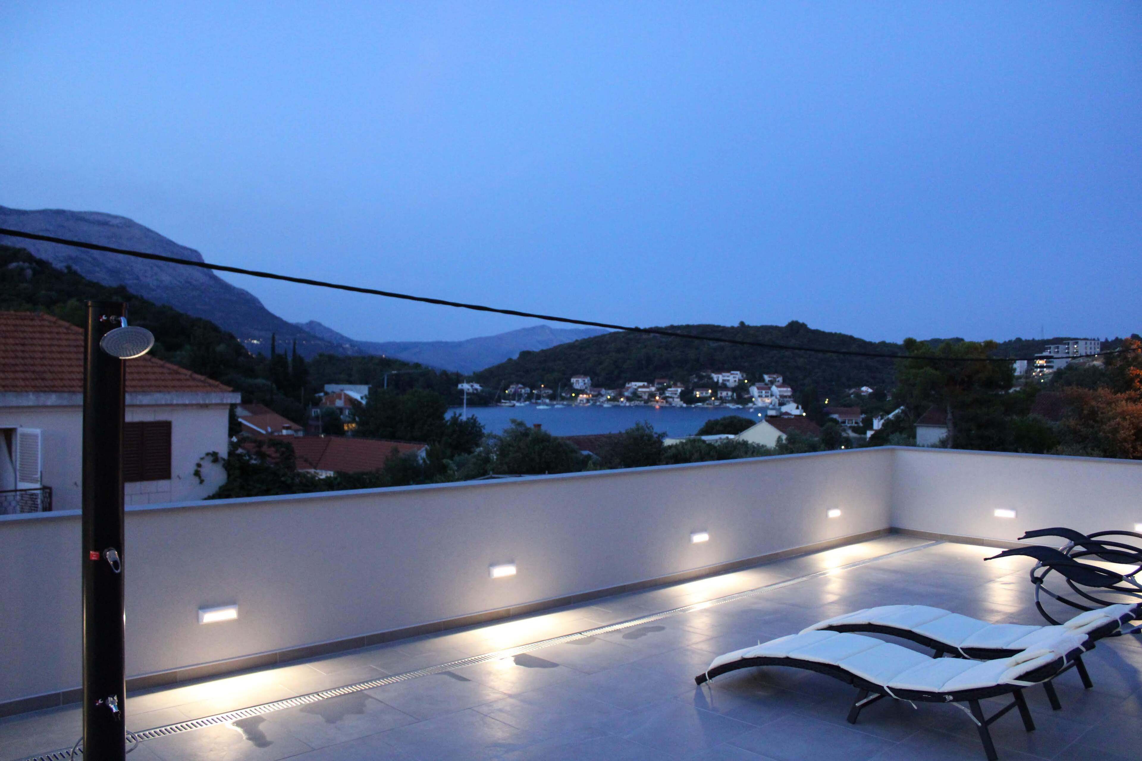 A rooftop terrace with lounge chairs and a view of a lake and mountains.