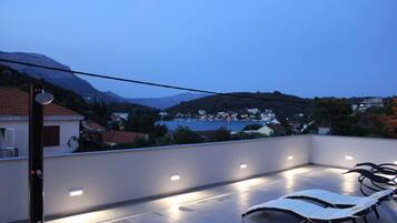 A rooftop terrace with lounge chairs and a view of a lake and mountains.