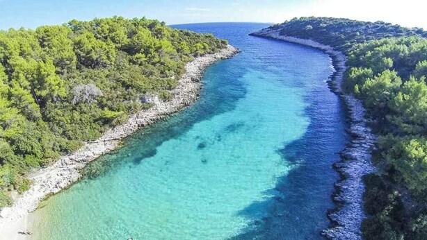 Eine Küstenlandschaft mit klarem türkisblauem Meer, felsiger Uferlinie und dichter, grüner Vegetation.