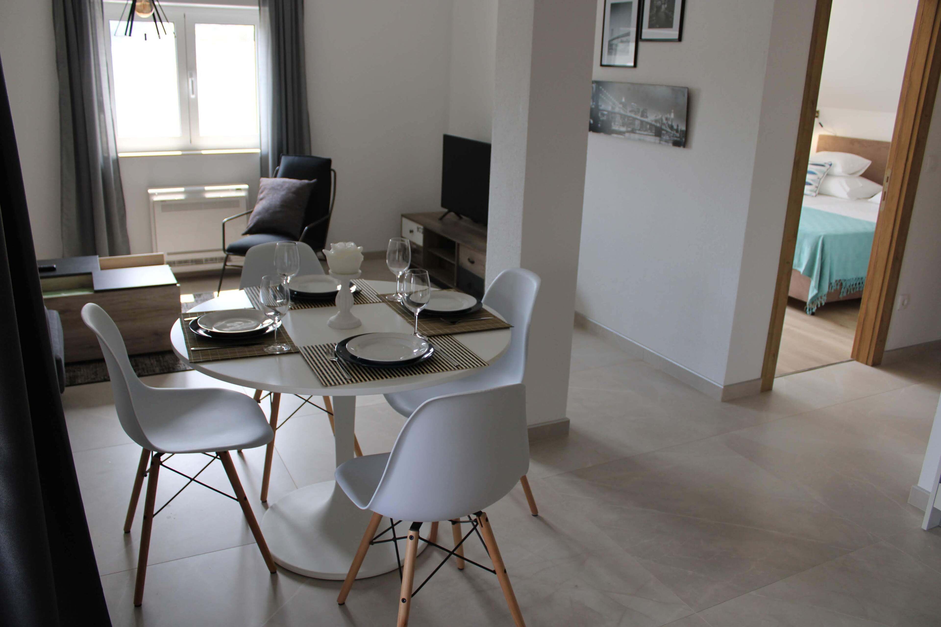 A dining area with a round table, white chairs, and a television in the background.