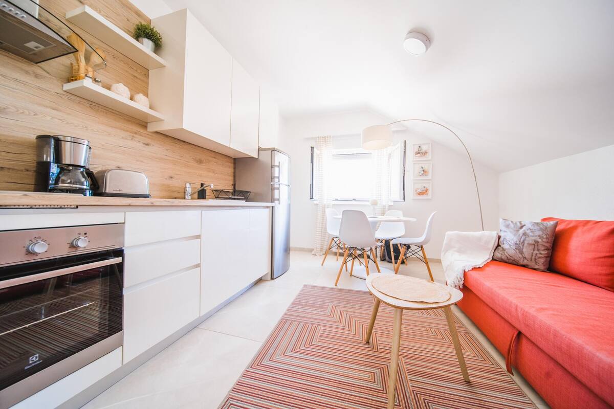 A modern kitchen with built-in appliances, a dining area with a table and chairs, and a red sofa in a bright living space.