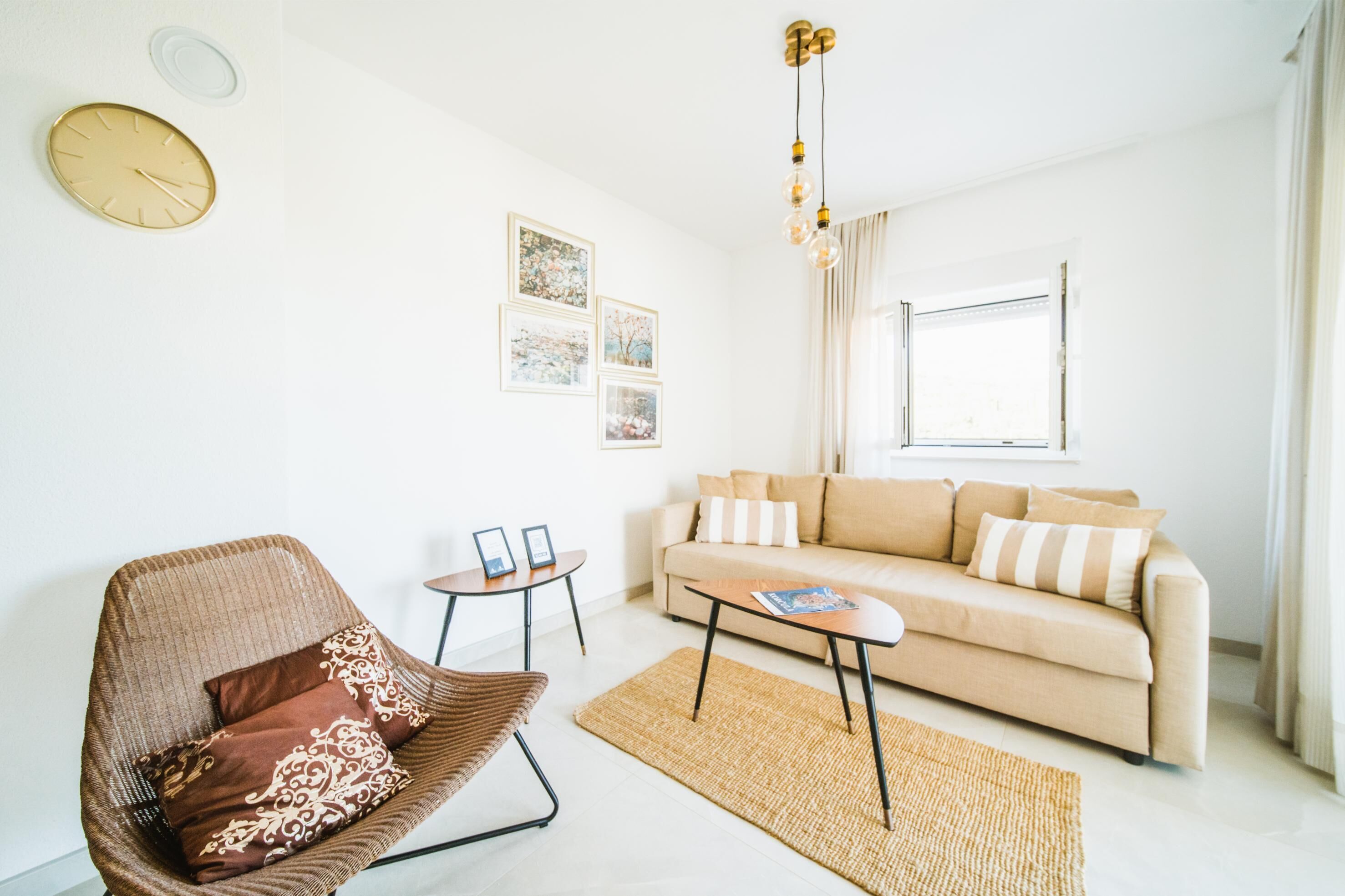 Uma sala de estar moderna com um sofá bege, uma poltrona marrom, uma mesa de centro e uma mesinha lateral com duas fotos emolduradas.