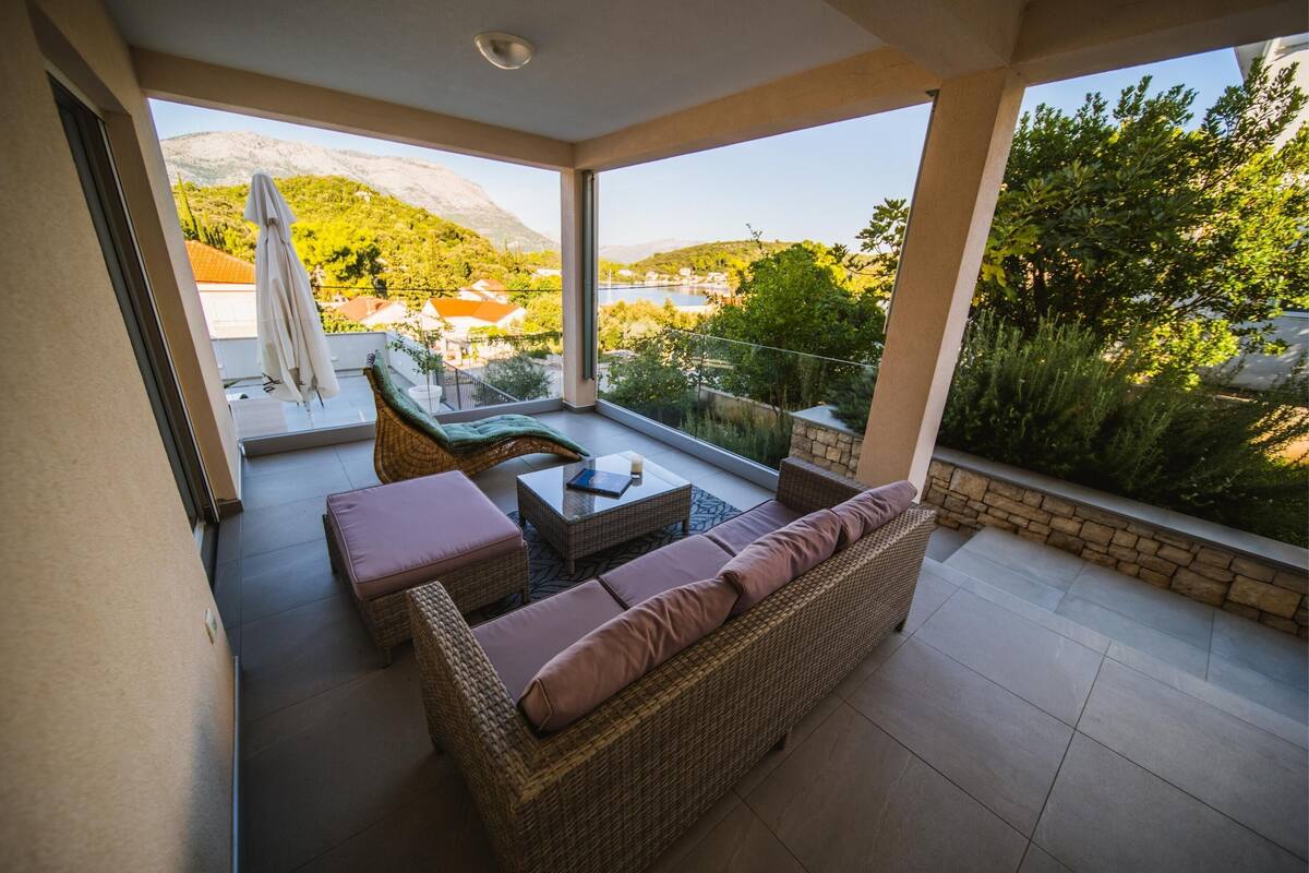A balcony with wicker furniture, a view of a lake, and a mountainous landscape.