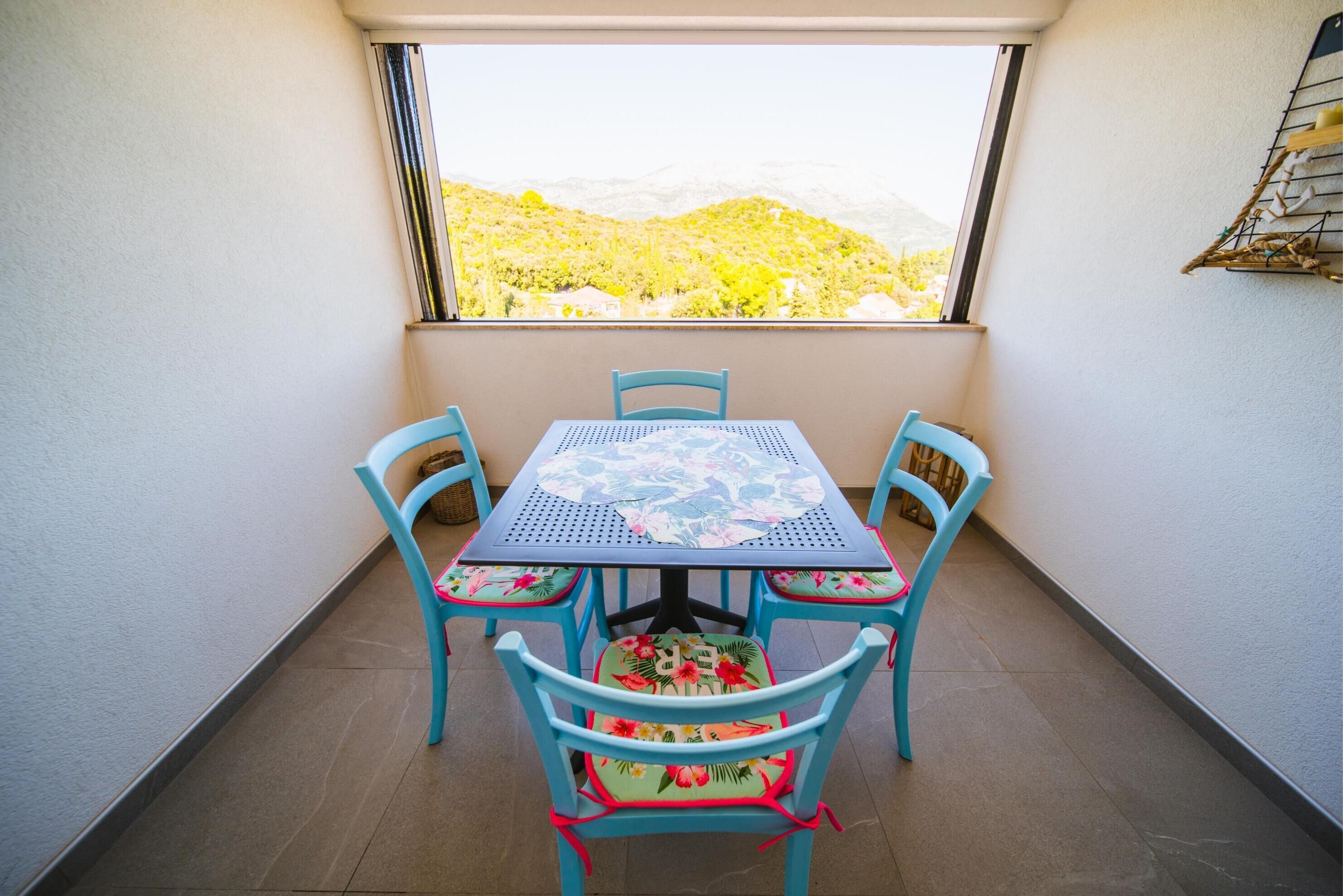 A balcony with a table and chairs, a view of a mountainous landscape through a window.