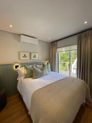 A bedroom with a large bed, a window with curtains, an air conditioning unit, and framed pictures on the wall. - Dieu Donné Vineyard Self-Catering Cottages (Franschhoek)