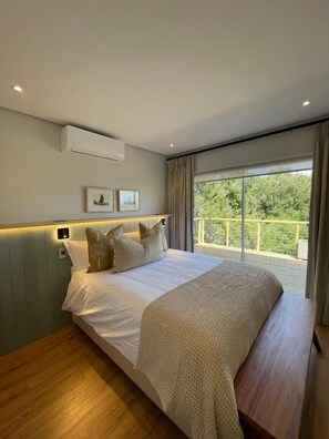 Une chambre avec un grand lit, une vue sur la verdure par la fenêtre et un balcon.
