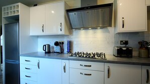 Una cocina moderna con armarios blancos, una campana extractora de acero inoxidable, una estufa a gas, un tostador y una tetera.