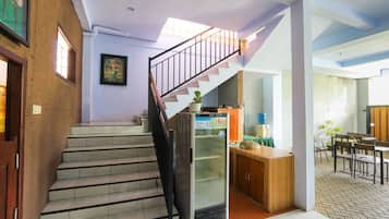 Un escalier menant à un deuxième étage, un réfrigérateur, un coin repas avec des chaises et des tables, et un mur orné d’un tableau encadré.