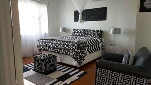 A bedroom with a bed, bedside lamps, a patterned rug, and a chair. - Campismo Ninho 39 (Ponta d'Ouro)
