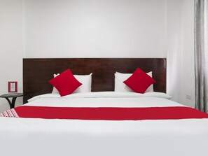 A hotel room with a large bed, two red pillows, a wooden headboard, and a small table with a red sign.