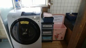 A front-loading washing machine and two storage bins labeled "Bath towel" and "Face towel" in a laundry area. - Ryu (Hatsukaichi)