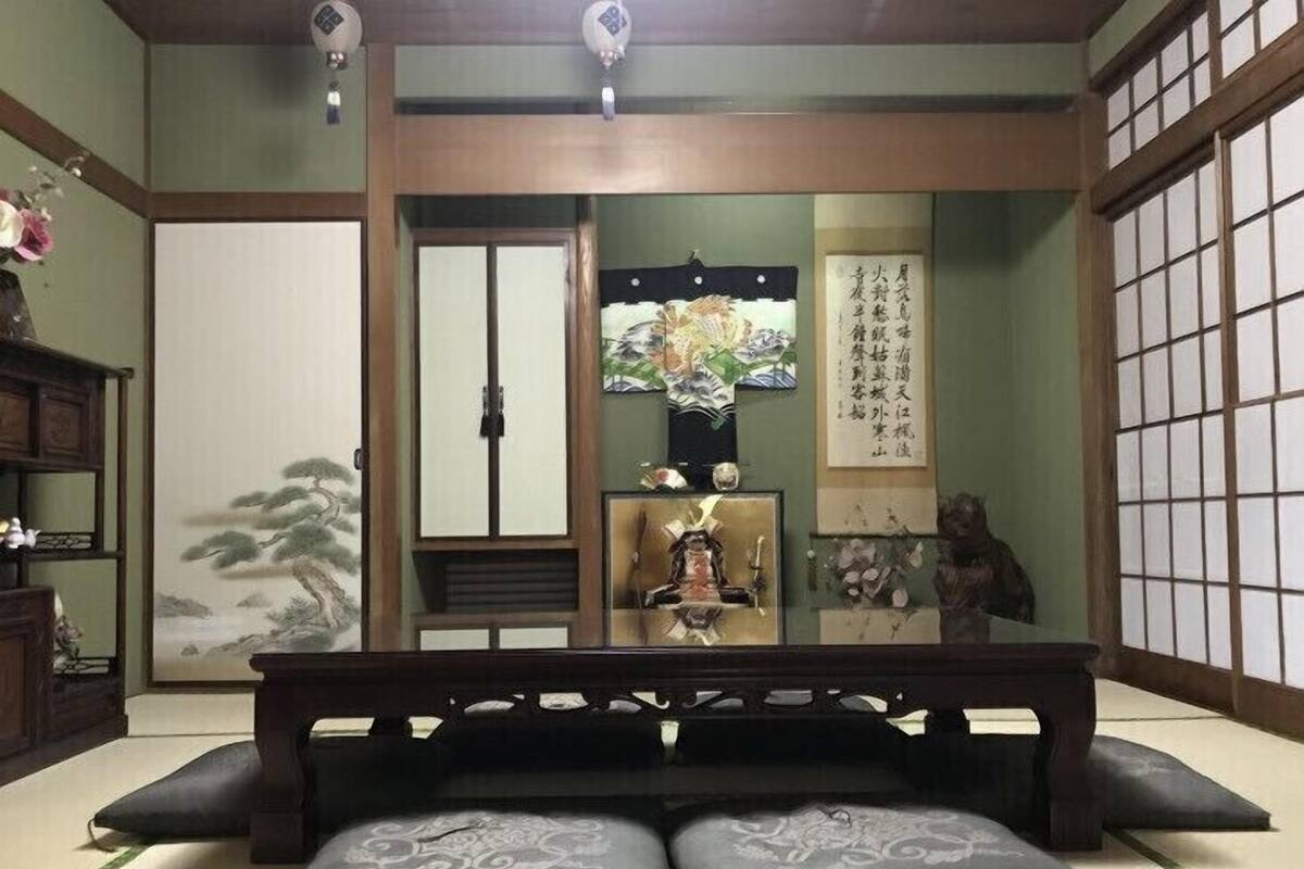 Una habitación japonesa tradicional con suelo de tatami, un banco de madera bajo, un separador shoji y un rollo de caligrafía.