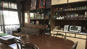 A dining area with a wooden table and chairs, a sofa, and a kitchen area with cabinets and appliances. - Ryu (Hatsukaichi)