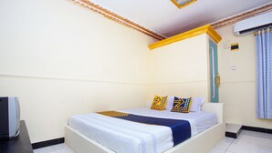 A single bed with a white and blue bedspread, two pillows with geometric patterns, and a small bedside table with a television. - Hotel O Buana Jaya Guest House (Cilacap)