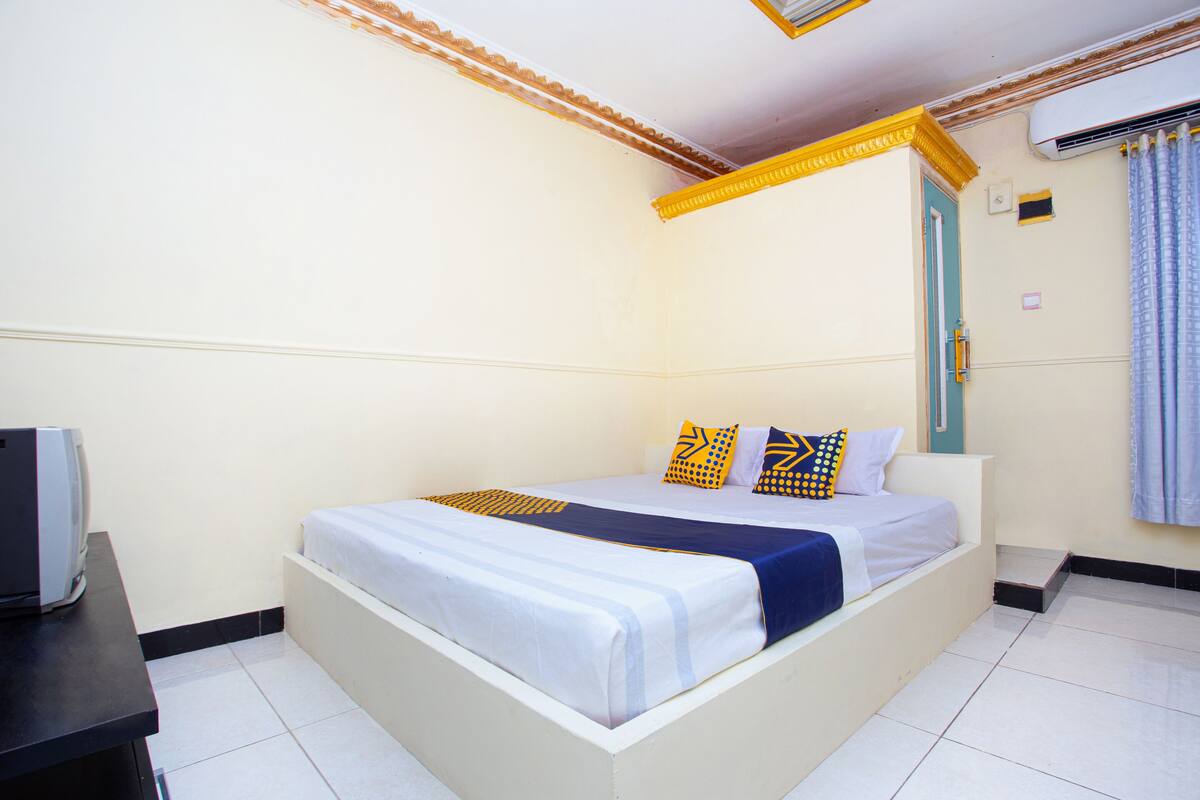 A single bed with a white and blue bedspread, two pillows with geometric patterns, and a small bedside table with a television.