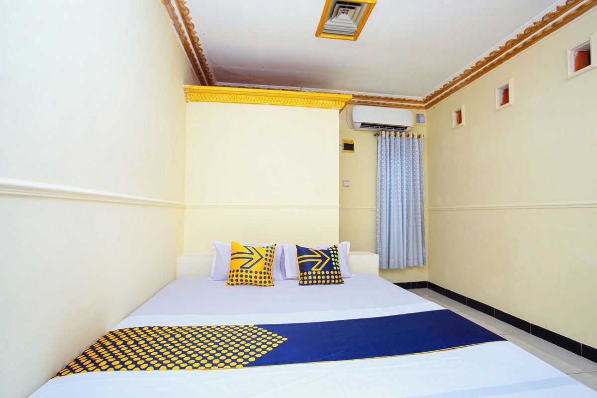 Habitación de hotel con cama, ventana con cortinas y aire acondicionado instalado en la pared.