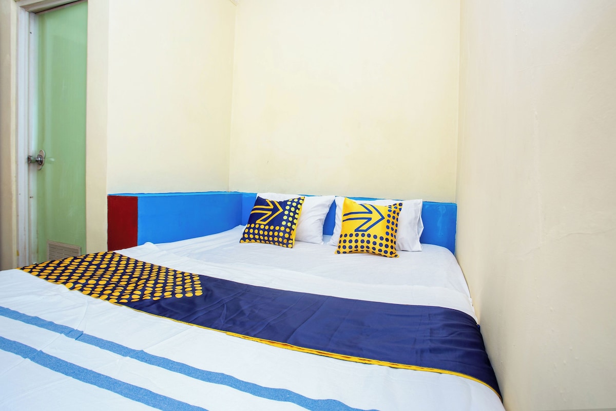 Una cama con una colcha azul y blanca a rayas, dos almohadas con diseños amarillos y azules, y un cabecero azul.