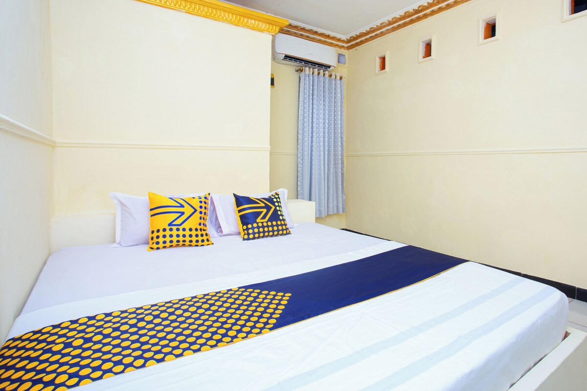 A neatly made bed with a blue and yellow patterned bedspread, white pillows, and a blue and yellow pillow on the headboard.