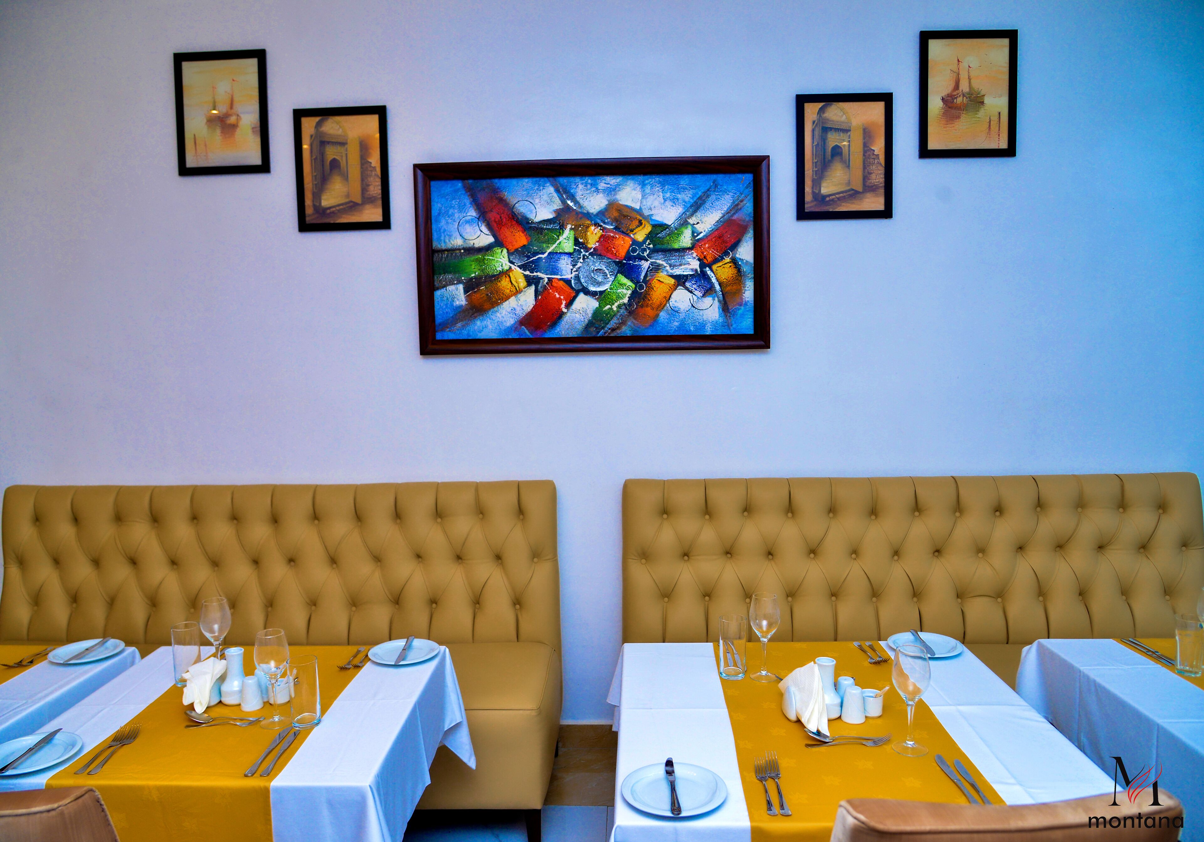 Un comedor con dos mesas dispuestas para dos comensales, cada una con mantel blanco, sillas con detalles dorados y cubertería ordenada.