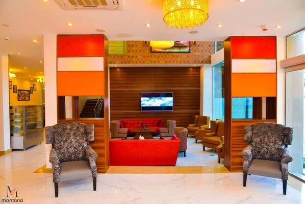 A lobby with a red sofa, two patterned armchairs, a television, and a chandelier.