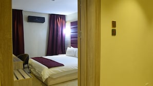 Habitación de hotel con cama, escritorio y silla. Se observa un aire acondicionado de pared y un interruptor de luz.