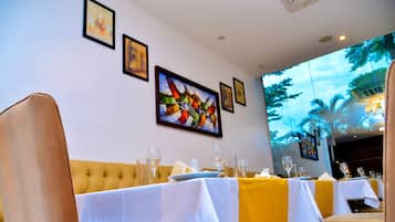 Comedor con mesas preparadas para dos, obras de arte en las paredes y una proyección de paisaje tropical.
