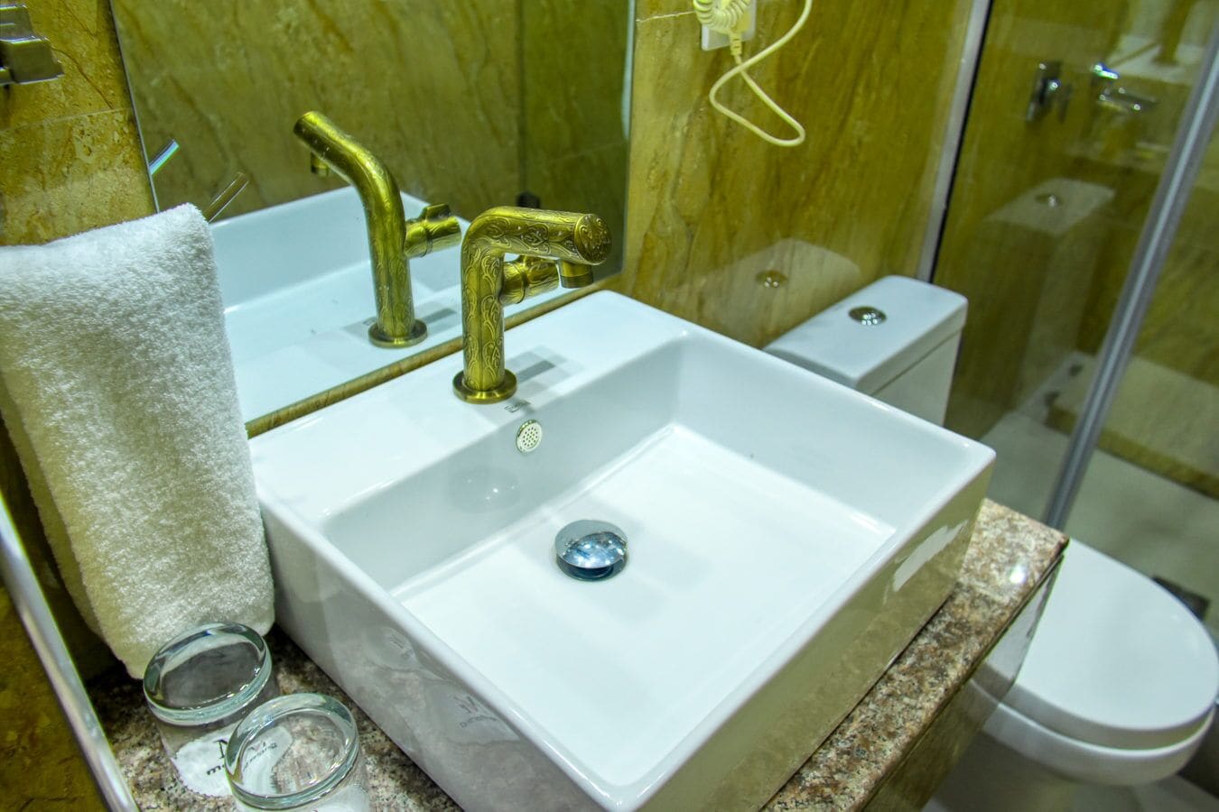Un baño con lavamanos blanco, grifos dorados, cabina de ducha de vidrio y un inodoro.