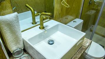 Un baño con lavamanos blanco, grifos dorados, cabina de ducha de vidrio y un inodoro.