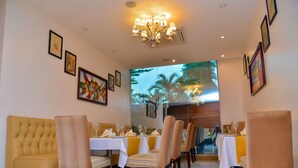 Un restaurante con zona de comedor que cuenta con mesas cubiertas con manteles blancos y servilletas amarillas, un sofá capitonado y una araña.