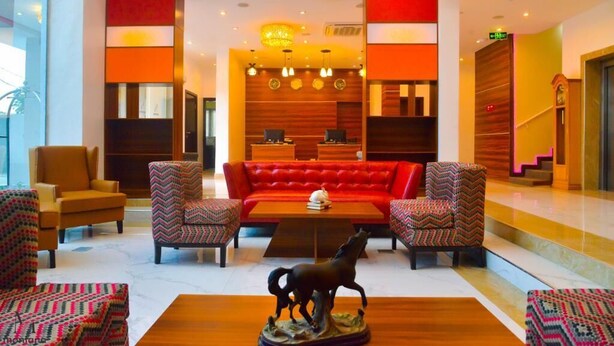 Un vestíbulo con un sofá rojo, sillas estampadas, una mesa de centro de madera y una estatua de un caballo.