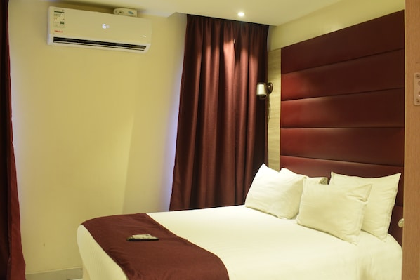 Een hotelkamer met een bed, een afstandsbediening op het bed, een wandairconditioner en een gordijn.