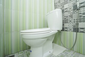 A toilet with a shower attachment in a bathroom with striped green and white tiles.