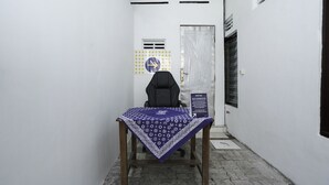 A narrow hallway with a table covered by a patterned tablecloth, a black office chair, and a sign on the wall. - Hotel O Berkah Residence Syariah (Gresik)
