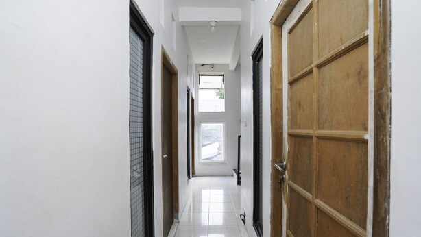 A corridor with white walls, a tiled floor, and wooden doors. - Hotel O Berkah Residence Syariah (Gresik)