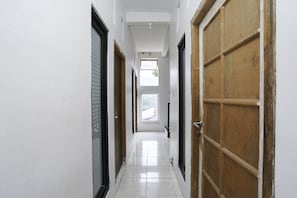 Un couloir aux murs blancs, doté d’un sol carrelé et de portes en bois.