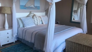 Un dormitorio con cama con dosel, una mesita de noche con lámpara, un cuadro en la pared y una cesta de mimbre.