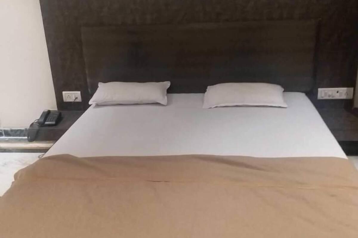 A bed with a dark headboard, two pillows, and a brown blanket.