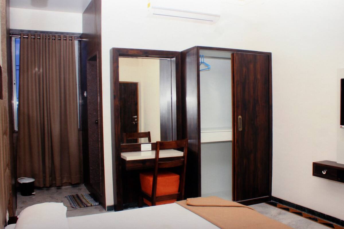 A bedroom with a bed, a wooden wardrobe, a chair, and a mirror.