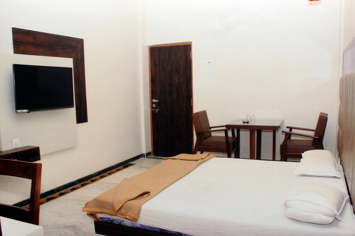 A hotel room with a bed, a TV mounted on the wall, a desk with two chairs, and a door.