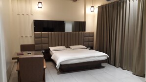 A modern bedroom with a large bed, a desk, and a chair. - Hotel Central Park (Ambernath)